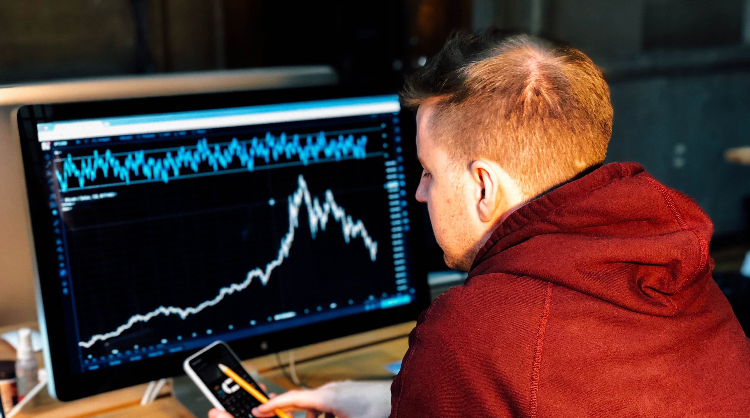 man looking at his phone with stock exchange graphs