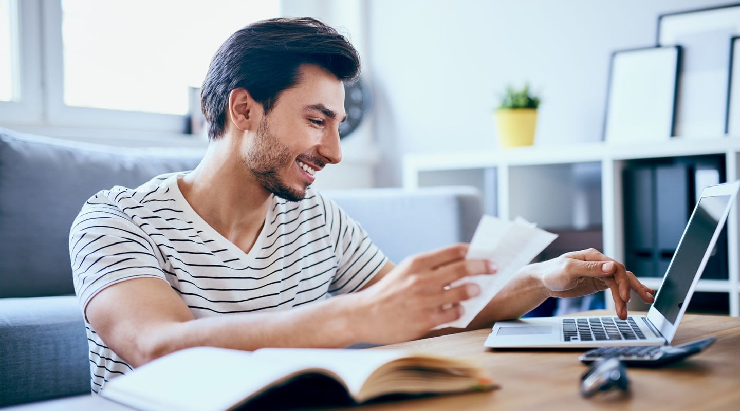 man smiling while checking his investments on laptop