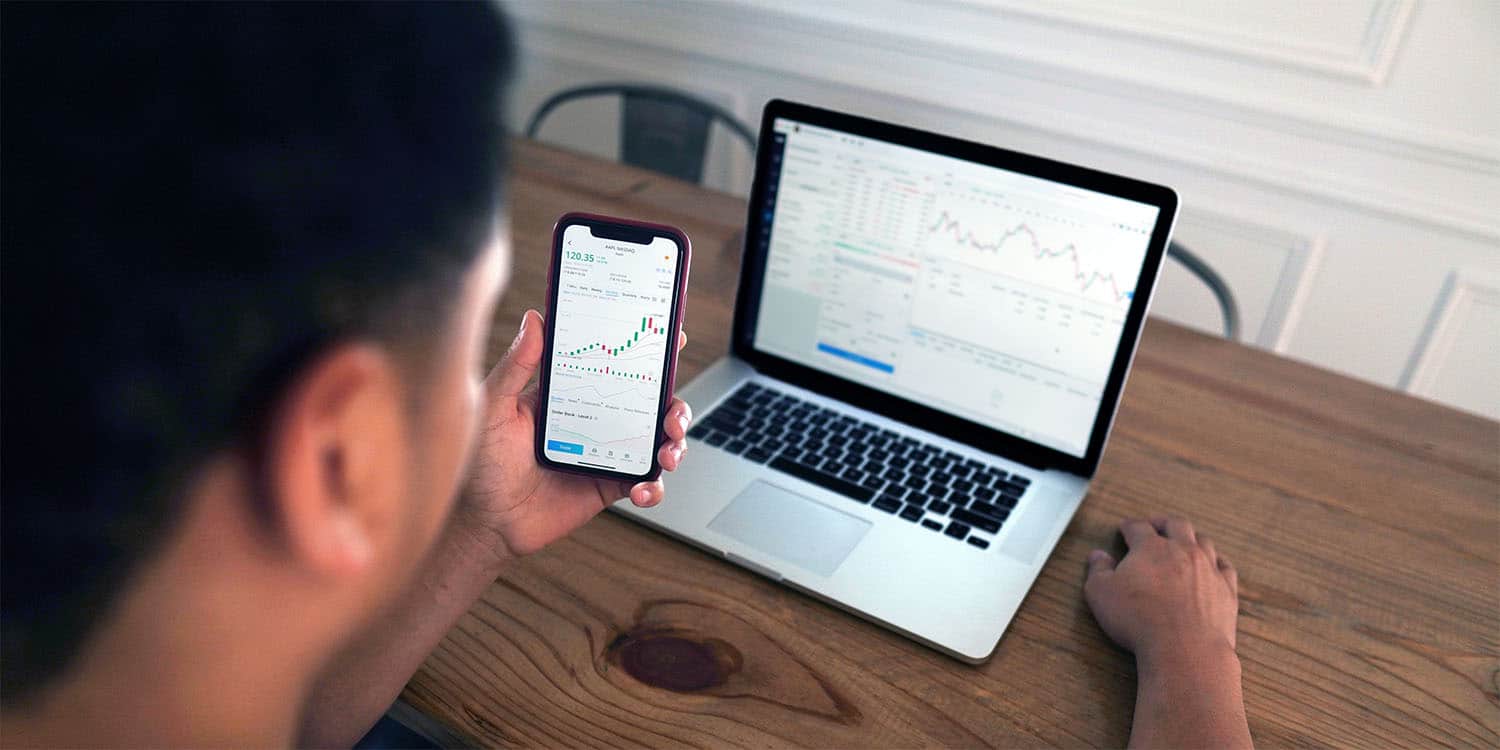 young man looking at stocks on phone and computer